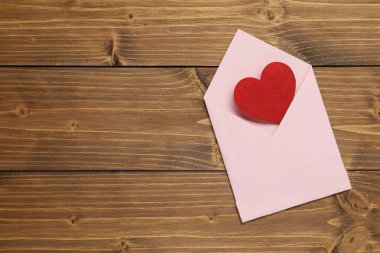 Sevgi. Ahşap zemin üzerinde kırmızı dekoratif kalp olan zarf, üst manzara. Metin için boşluk