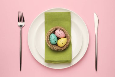 Paskalya kutlaması. Pembe arka planda boyalı yumurta ve çatal bıçaklı şenlik masası.