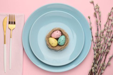 Paskalya kutlaması. Renkli yumurtalar, söğüt dalları ve pembe arka planda çatal bıçak seti olan şenlik masası.