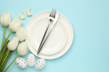 Paskalya kutlaması. Çatal bıçak takımları, laleler ve açık mavi arka planda boyanmış yumurtalar, düz yatak. Metin için boşluk