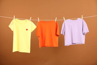 Çamaşır ipini kahverengi arka planda tutarken farklı giysiler kuruyor.