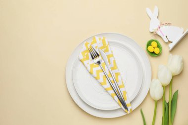 Paskalya kutlaması. Renkli yumurtalar, lale çiçekleri ve bej arka planda çatal bıçak takımlarıyla şenlik masası, metin için yeri olan düz bir yer.