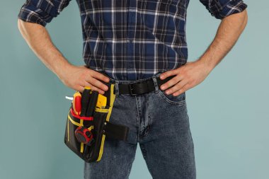 Açık mavi arka planda alet kemeri olan profesyonel inşaatçı, yakın plan