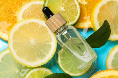 Bir şişe cilt bakımı ürünü, narenciye dilimleri ve açık mavi arka planda yeşil yapraklar.