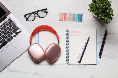Kulaklıklar, dizüstü bilgisayarlar, gözlükler, kırtasiye malzemeleri ve beyaz mermer masa üzerindeki çiçek dekoru, düz konum.