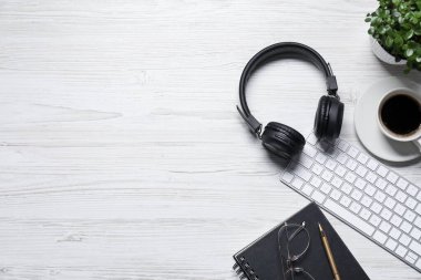 Kulaklıklar, bilgisayar klavyesi, kahve, çiçek dekoru, beyaz ahşap masadaki kırtasiye malzemeleri, düz yatak. Metin için boşluk
