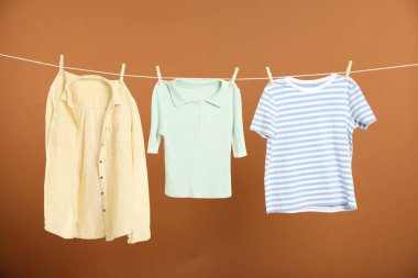 Çamaşır ipini kahverengi arka planda tutarken farklı giysiler kuruyor.