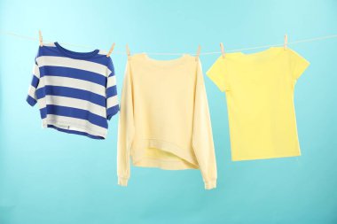 Açık mavi arka planda çamaşır ipine tutunurken farklı giysiler kuruyor