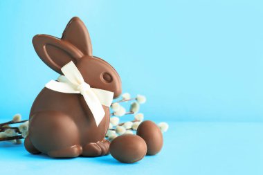 Çikolatalı Paskalya tavşanı, açık mavi arka planda yumurta ve söğüt dalları, yakın plan. Metin için boşluk