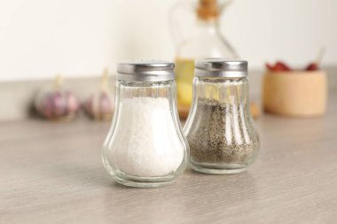 Beyaz duvarın yanındaki ahşap masada baharatlı tuzluk ve biberlikler.