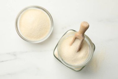 Kavanozda jelatin tozu, kepçe ve kase beyaz masada, düz yerde.