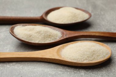 Açık gri masada kaşıklarda jelatin tozu, yakın plan.