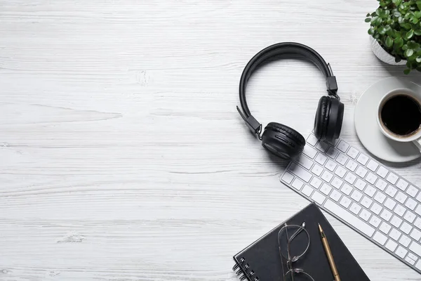 Kulaklıklar, bilgisayar klavyesi, kahve, çiçek dekoru, beyaz ahşap masadaki kırtasiye malzemeleri, düz yatak. Metin için boşluk