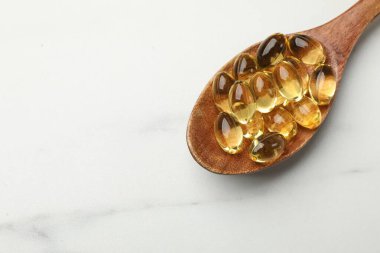 Beyaz masada kaşıkta altın jelatin kapsüller, üst manzara. Metin için boşluk