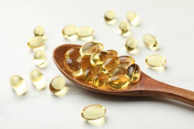 Altın jelatin kapsüller ve kaşık beyaz masada, yakın plan.