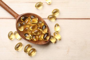 Kaşık içinde altın jelatin kapsüller beyaz ahşap masada, yakın plan