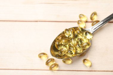 Beyaz ahşap masada kaşıkta altın jelatin kapsüller, yakın plan. Metin için boşluk