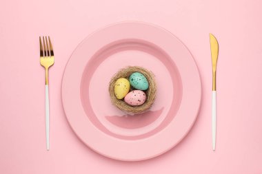 Paskalya kutlaması. Pembe arka planda boyalı yumurta ve çatal bıçaklı şenlik masası.