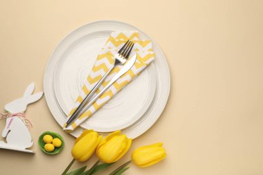 Paskalya kutlaması. Renkli yumurtalar, lale çiçekleri ve bej arka planda çatal bıçak takımlarıyla şenlik masası, metin için yeri olan düz bir yer.