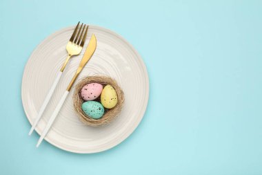 Paskalya kutlaması. Çatal bıçak takımı ve açık mavi arka planda boyalı yumurtalar, üst manzara. Metin için boşluk
