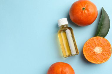 Bir şişe mandalina yağı ve açık mavi arka planda meyveler. Metin için boşluk