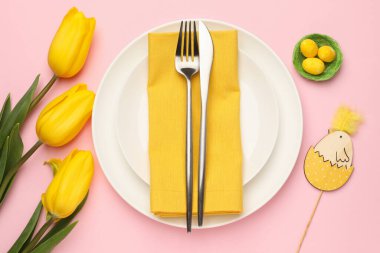 Paskalya kutlaması. Renkli yumurtalar, lale çiçekleri ve pembe arka planda çatal bıçak seti olan şenlik masası.