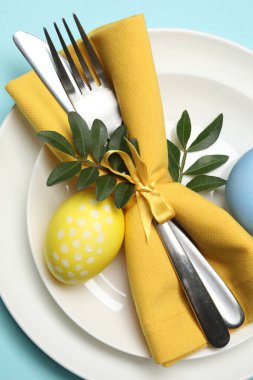 Paskalya kutlaması. Yeşil yaprakları ve açık mavi arka planda boyanmış yumurtaları olan şenlikli masa ayarı, üst manzara.