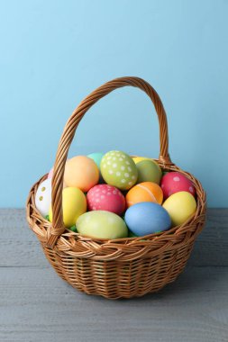 Hasır sepetin içine boyanmış Paskalya yumurtaları açık mavi arka plana karşı gri ahşap masa üzerinde
