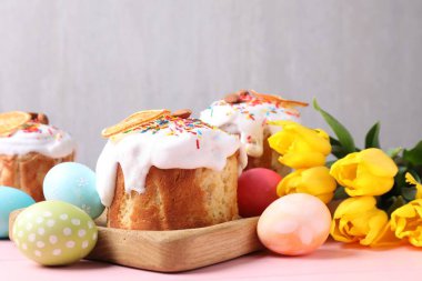 Lezzetli Paskalya pastaları, laleler ve pembe masanın üzerine boyanmış yumurtalar.