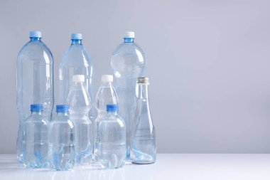 Beyaz masada gri arkaplan ile farklı boyutlarda su şişeleri, metin için boşluk