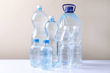 Beyaz masada bej arka planda farklı boyutlarda su şişeleri