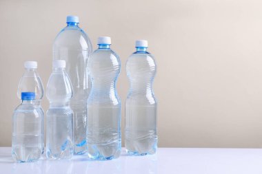 Beyaz masada bej arka planda farklı boyutlarda su şişeleri var. Metin için boşluk
