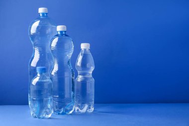 Mavi arka planda farklı boyutlarda su şişeleri var. Metin için boşluk
