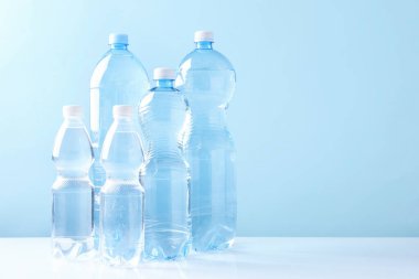 Beyaz masada açık mavi arka planda farklı boyutlarda su şişeleri var. Metin için boşluk