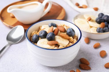 Yulaf gevreği, badem sütü, fındık, muz ve yaban mersini açık gri masada, yakın plan.