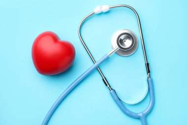 Açık mavi arka planda steteskop ve kalp modeli, üst görünüm