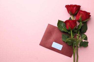 Zarfta boş etiket ve pembe arka planda kırmızı güller var. Metin için boşluk