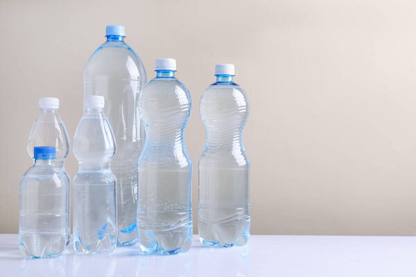 Water bottles of different sizes on white table against beige background. Space for text
