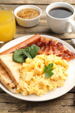 Lezzetli bir kahvaltı. Lezzetli çırpılmış yumurta, domuz pastırması ve sosis, ahşap masada servis edilir, yakın plan.