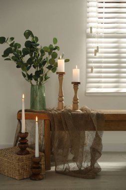 Zarif şamdanlar, yanan mumlar ve kapalı masa üzerinde dalları olan vazolar.