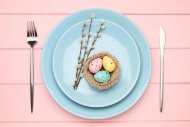 Paskalya kutlaması. Çatal bıçak seti, söğüt dalları ve pembe ahşap masa üzerine boyanmış yumurtalarla süslü bir yer.