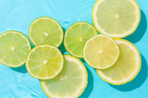 Açık mavi zemin üzerinde limon ve limon dilimleri, düz uzanmış.