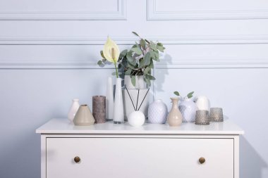 Beyaz duvarın yanındaki dolapta güzel vazolar ve diğer dekorlar var.