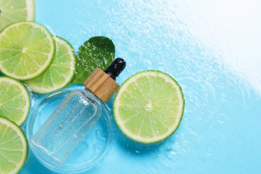 Bir şişe cilt bakımı ürünü, limon dilimleri ve açık mavi arkaplanda yeşil yaprak, düz bir zemin. Metin için boşluk