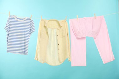 Açık mavi arka planda çamaşır ipine tutunurken farklı giysiler kuruyor