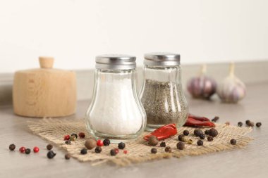 Beyaz duvarın yanındaki ahşap masada baharatlı tuzluk ve biberlikler.