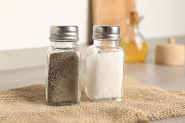 Beyaz duvarın yanındaki ahşap masada baharatlı tuzluk ve biberlikler.