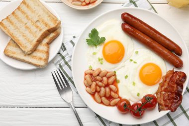 Geleneksel İngiliz kahvaltısı. Lezzetli, güneşli, domuz pastırmalı yumurta ve sosisler beyaz ahşap masada servis ediliyor.
