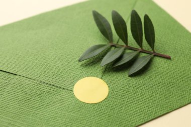 Boş yapıştırmalı zarf ve bej arkaplanda yeşil yapraklar, yakın plan