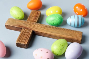 Ahşap haç ve açık gri arka planda Paskalya yumurtaları, yakın plan.